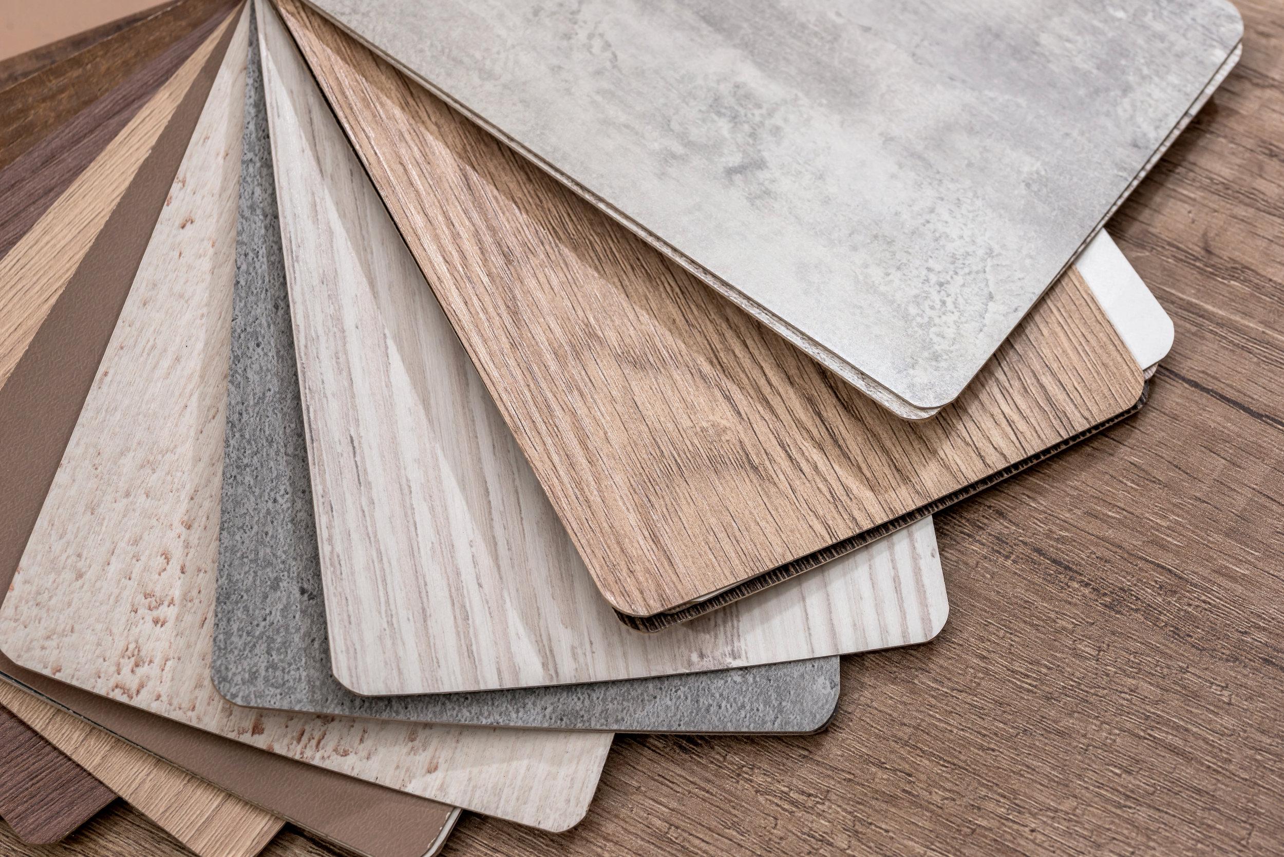 A fan of LVT and hardwood-look flooring samples on a wood surface.