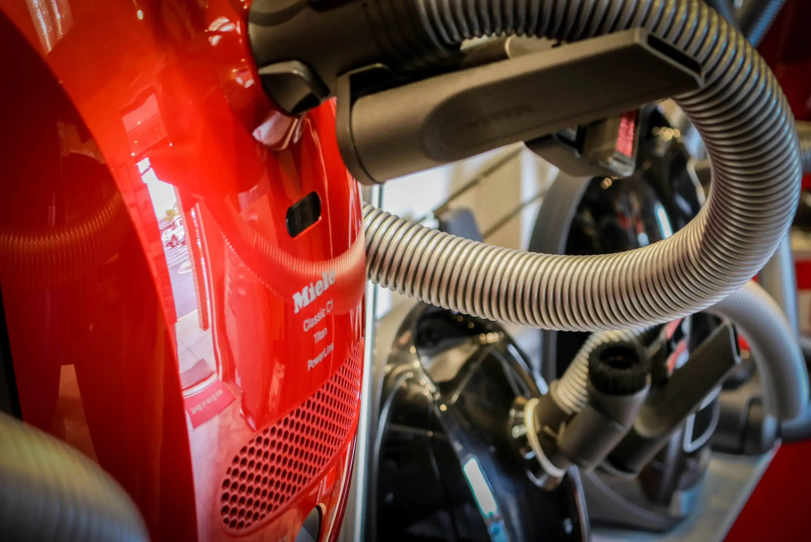 Miele Classic C1 canister on the Olney showroom shelf, with additional Miele canister units lined up behind it and a coiled hose in the foreground.